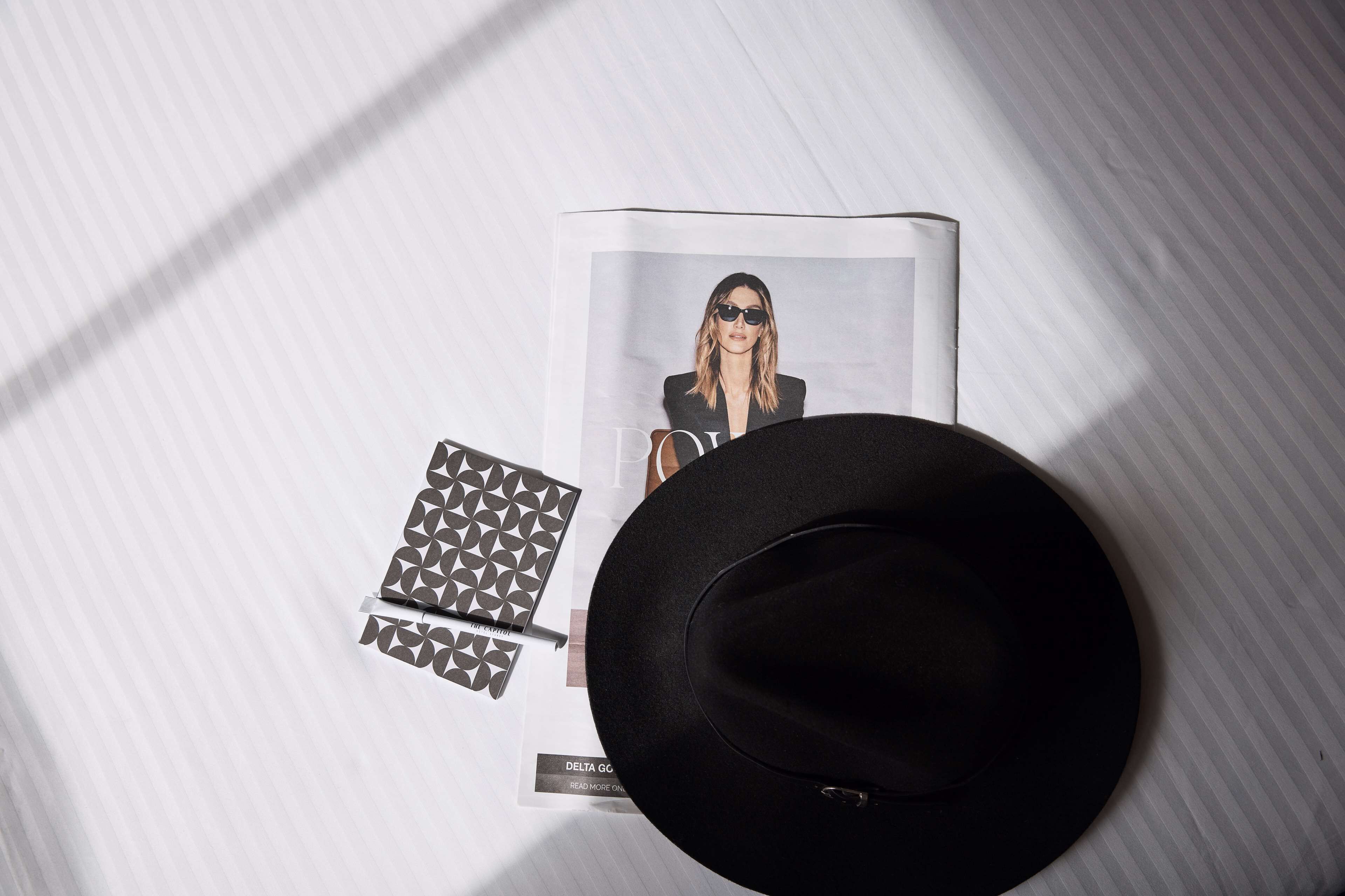 A black hat, a magazine with a photo of a woman, and a geometric-patterned notebook on a white surface.