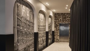 A hallway with ornate wall panels, a brick wall, and a modern elevator. - The Capitol Hotel Sydney (Haymarket)