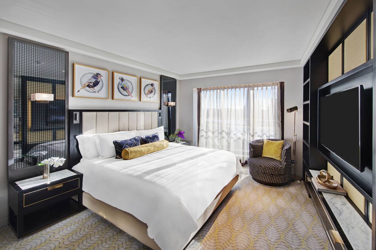 A hotel room with a large bed, a TV, a chair, and artwork on the walls.