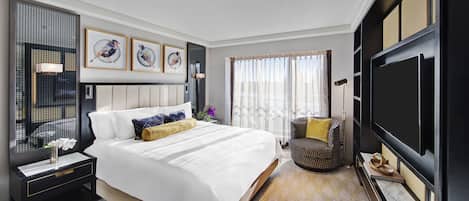 A hotel room with a large bed, a TV, a chair, and artwork on the walls.