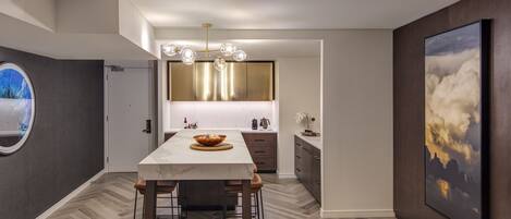 A modern kitchen with a marble countertop, wooden stools, and a central island.