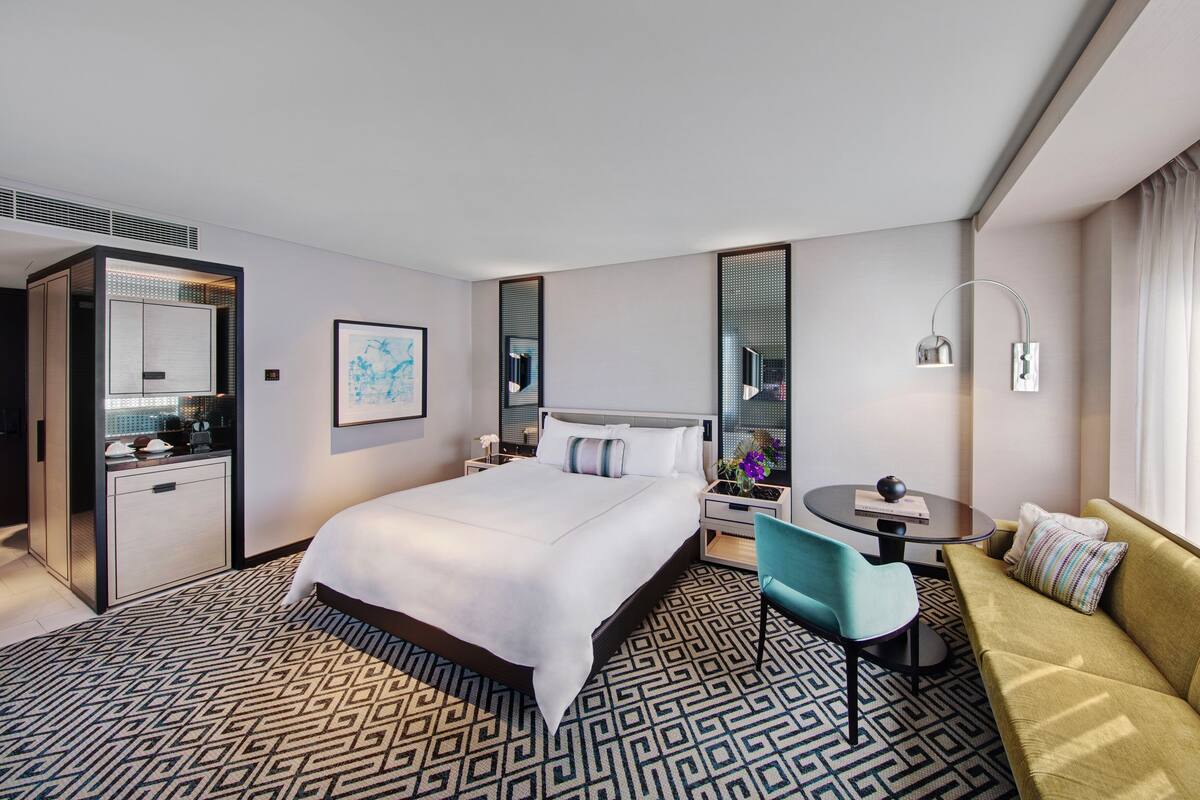 A modern hotel room with a large bed, a desk, a chair, and a sofa.