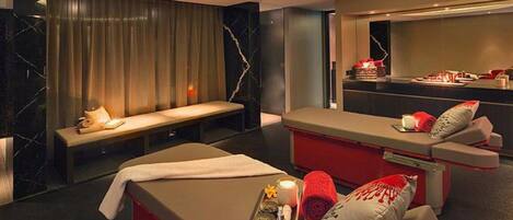 A modern spa room with a massage table, a bench, and a reception area with a counter and decorative items.