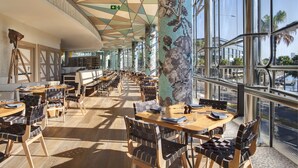 A spacious indoor dining area with high ceilings, large windows, and modern furniture.