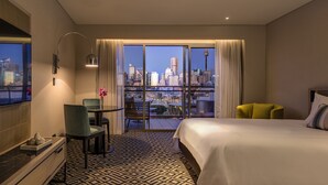 A hotel room with a city view, a bed, a desk, and a chair.