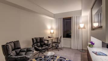 A hotel room with a round carpet, a desk, two chairs, a mirror, and a window with curtains.