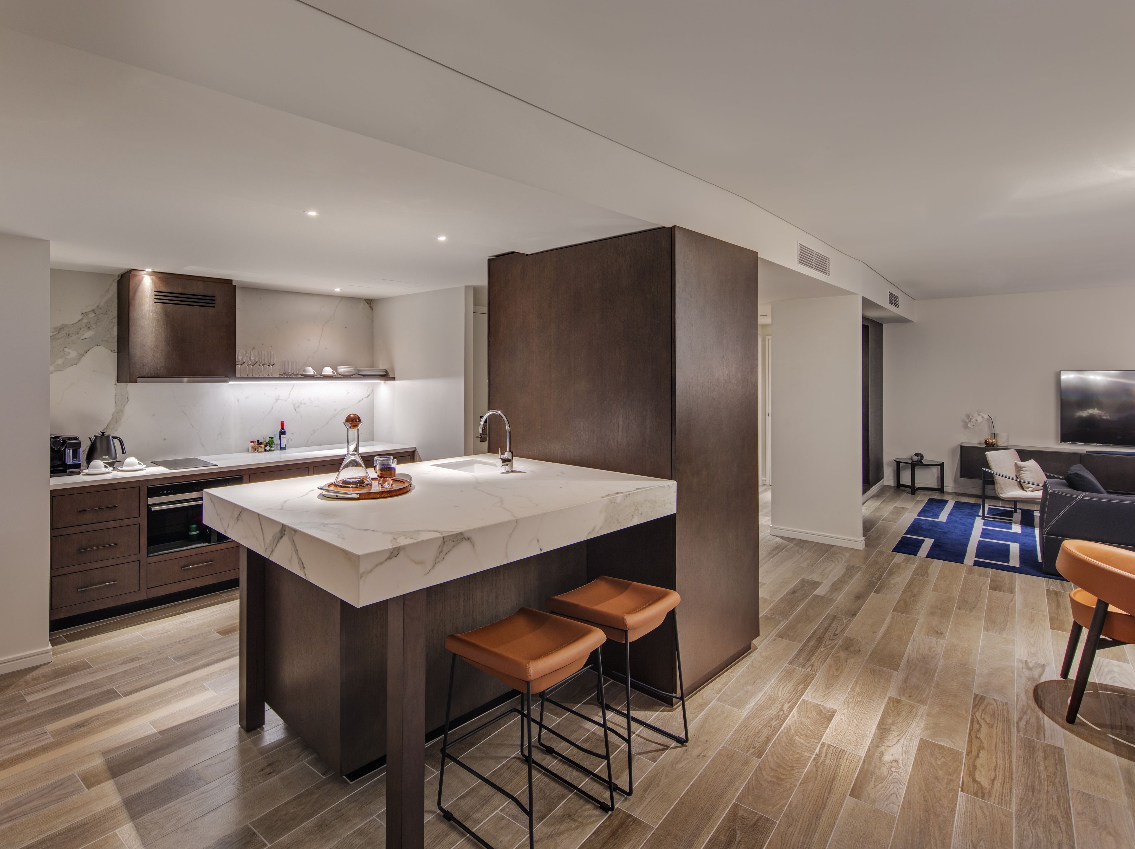 A modern kitchen with a marble countertop, dark cabinetry, and a built-in island with stools.