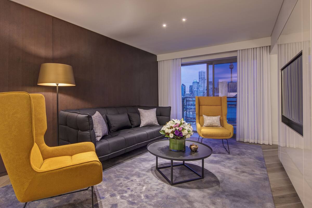 A modern living room with a sofa, two armchairs, a coffee table, and a city view through large windows.
