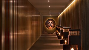 A corridor with a modern design, featuring a patterned wall on the left and a series of square platforms with candles on the right.
