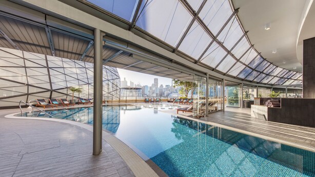 An indoor swimming pool with a city skyline view, lounge chairs, and a reception area.