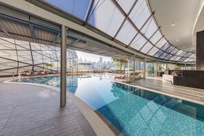 Piscina interna con vista sullo skyline cittadino, sedie a sdraio e area reception.