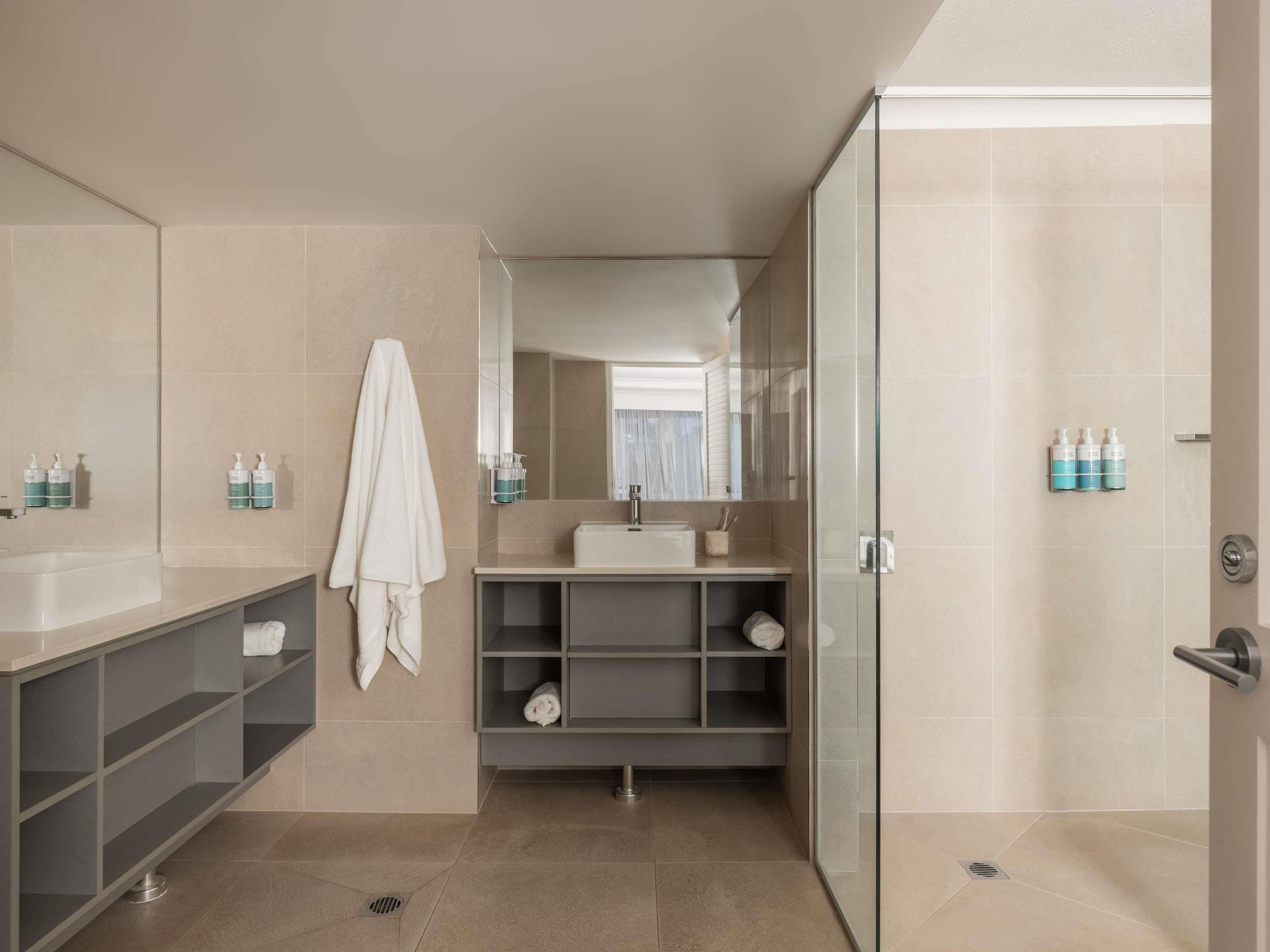 A modern bathroom with a glass shower enclosure, a large mirror, and a vanity with a sink and storage.