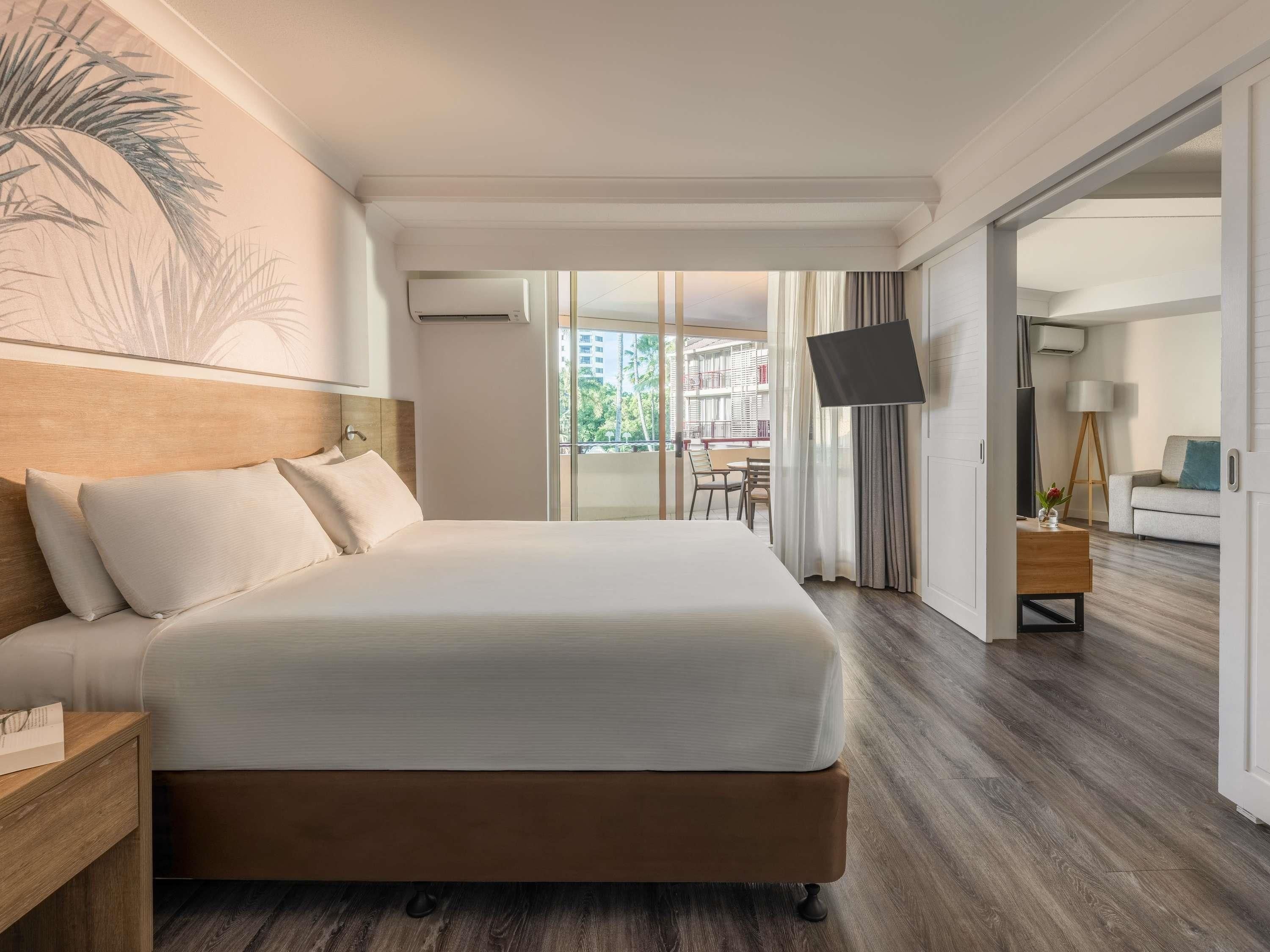 Ein Hotelzimmer mit einem großen Bett, einem Flachbildfernseher, einem Holz-Kopfteil und Blick auf den Außenbalkon.