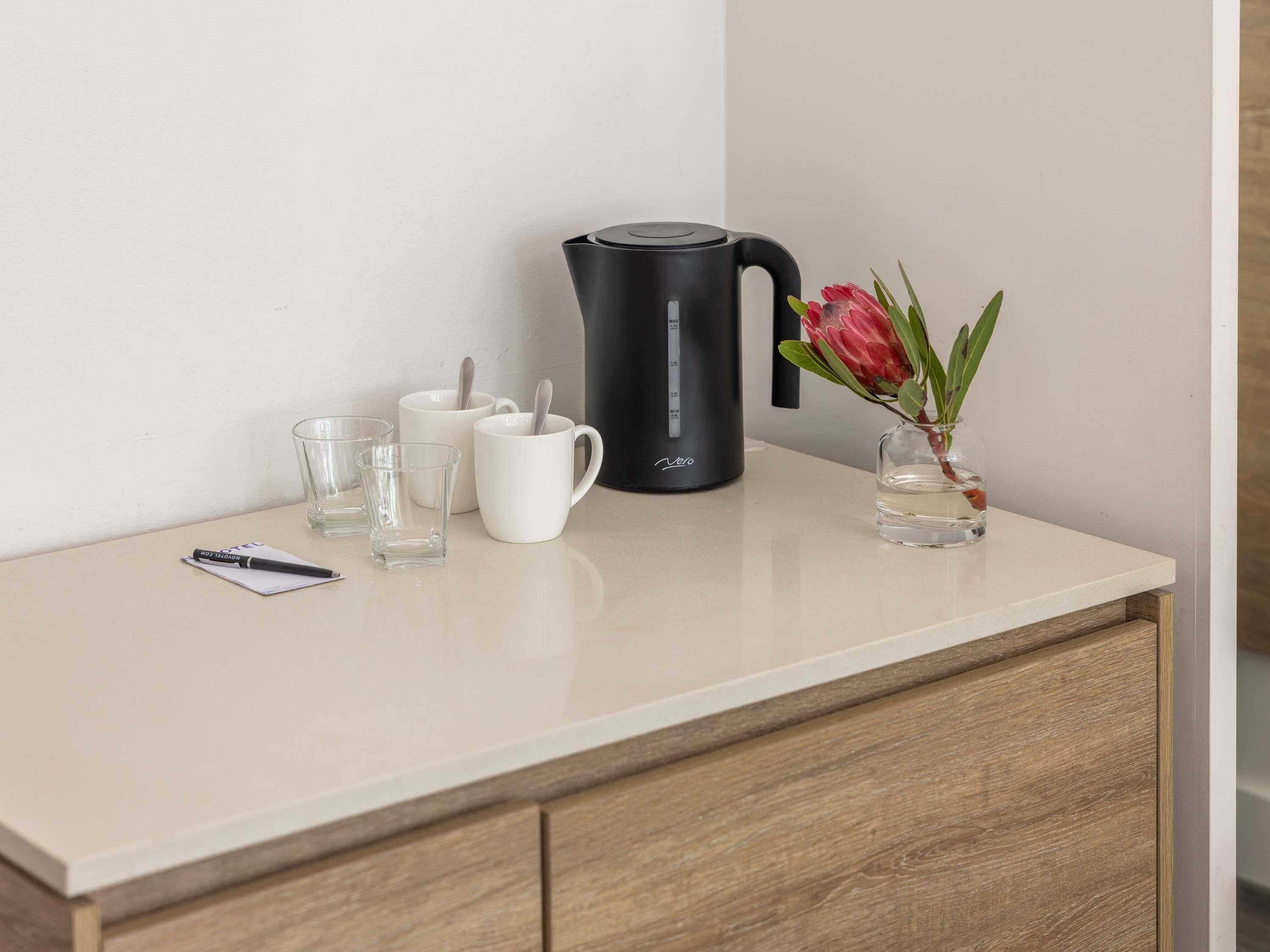 A kitchen counter with a coffee maker, a vase with a flower, and a pen on a notepad.