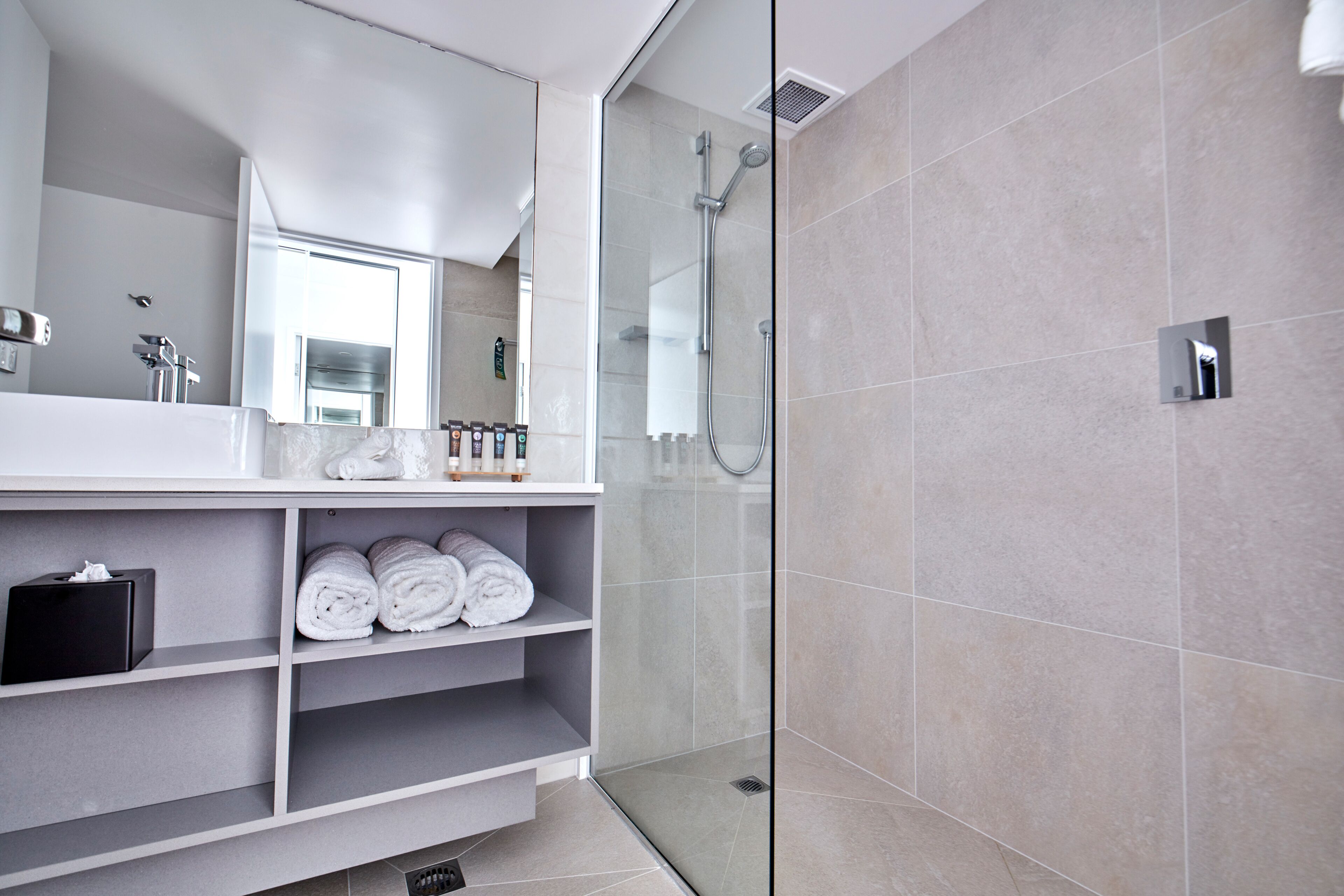 A modern bathroom with a glass-enclosed shower, a large mirror, and neatly folded towels on shelves.