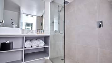 A modern bathroom with a glass-enclosed shower, a large mirror, and neatly folded towels on shelves.