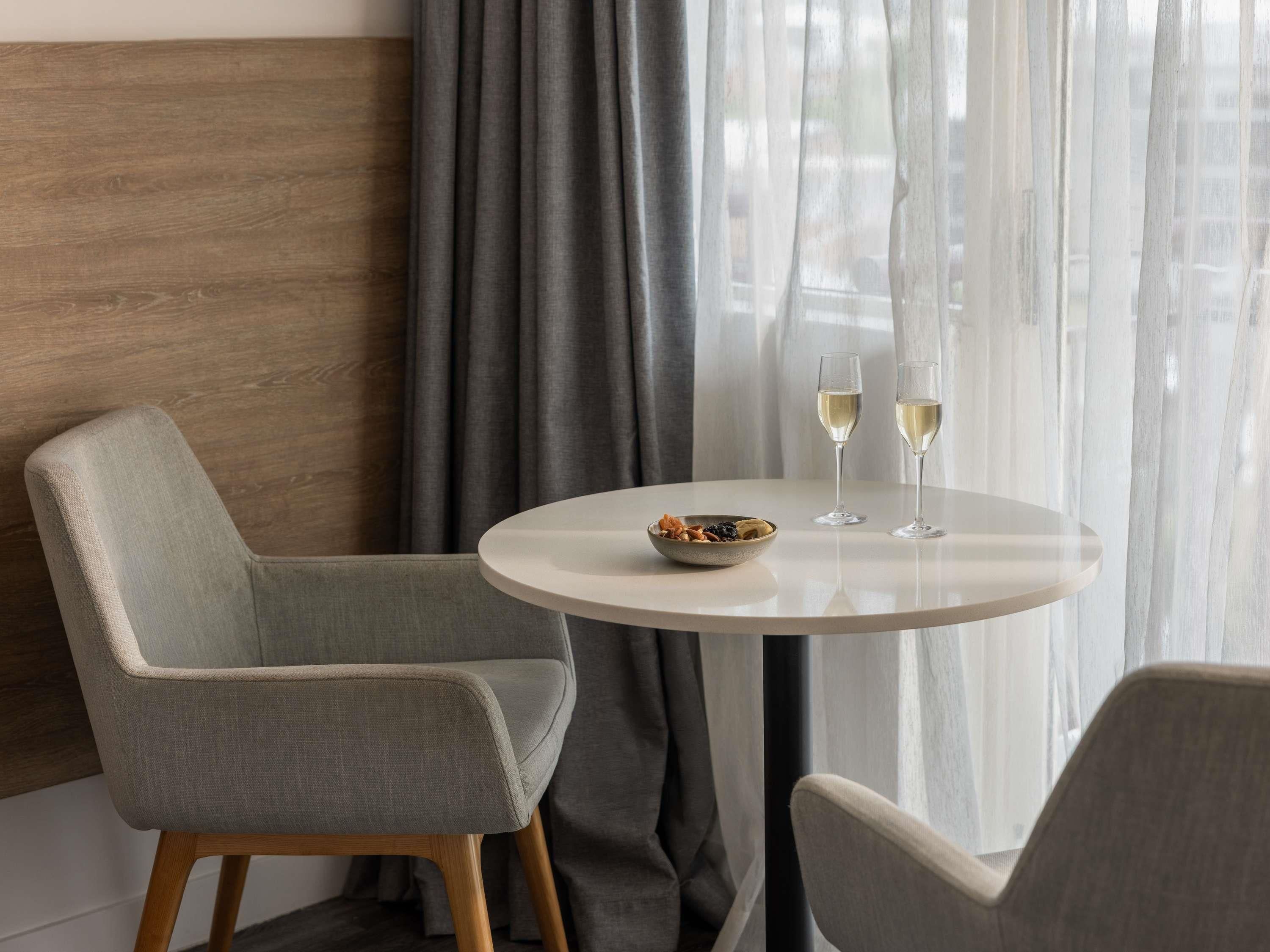 A modern dining area with two chairs, a round table, and two glasses of white wine.