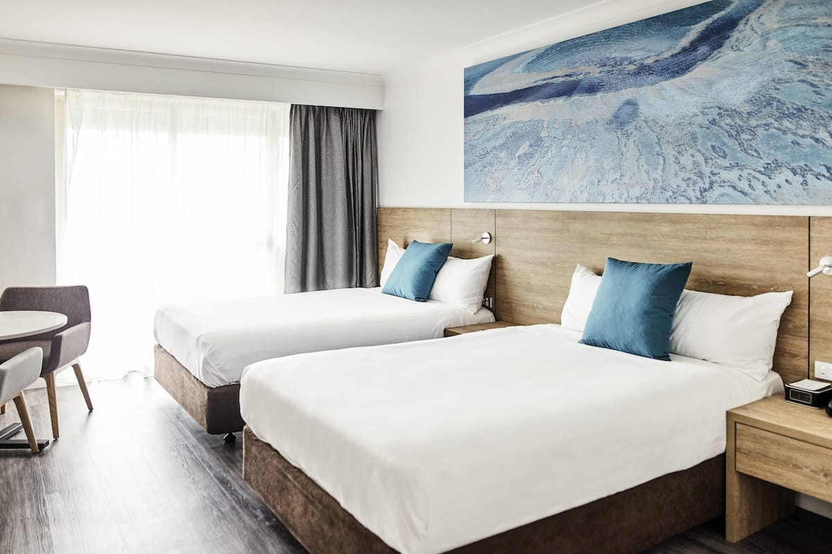 A hotel room with two beds, a desk, and a large abstract painting on the wall.