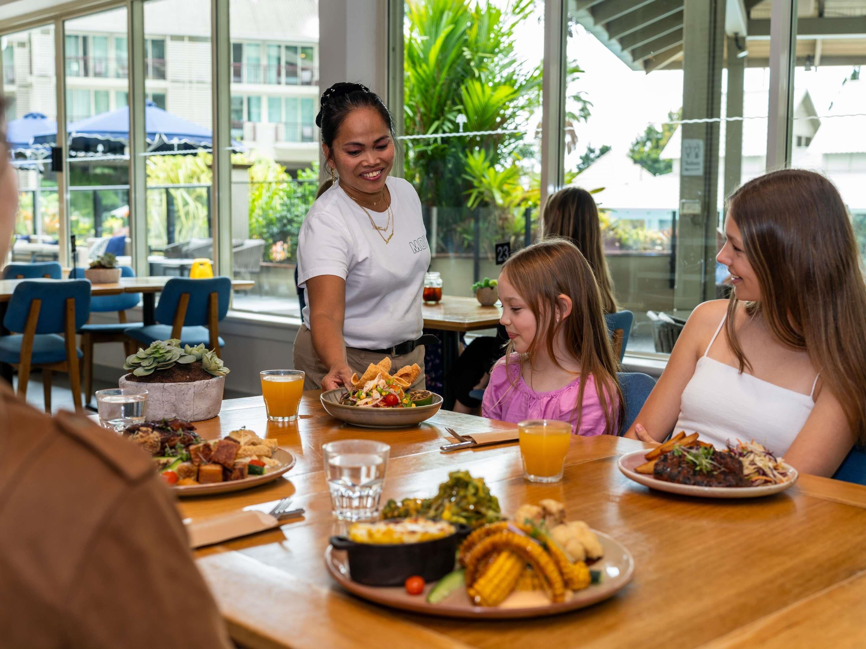 A restaurant with a modern interior, large windows, and a variety of dishes on the tables.