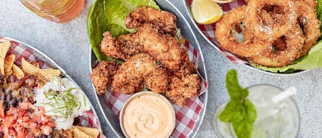 A variety of fried foods including chicken, onion rings, and chips, served with dipping sauces and garnishes.