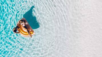 An aerial view of a beach with clear water and a person on a float.