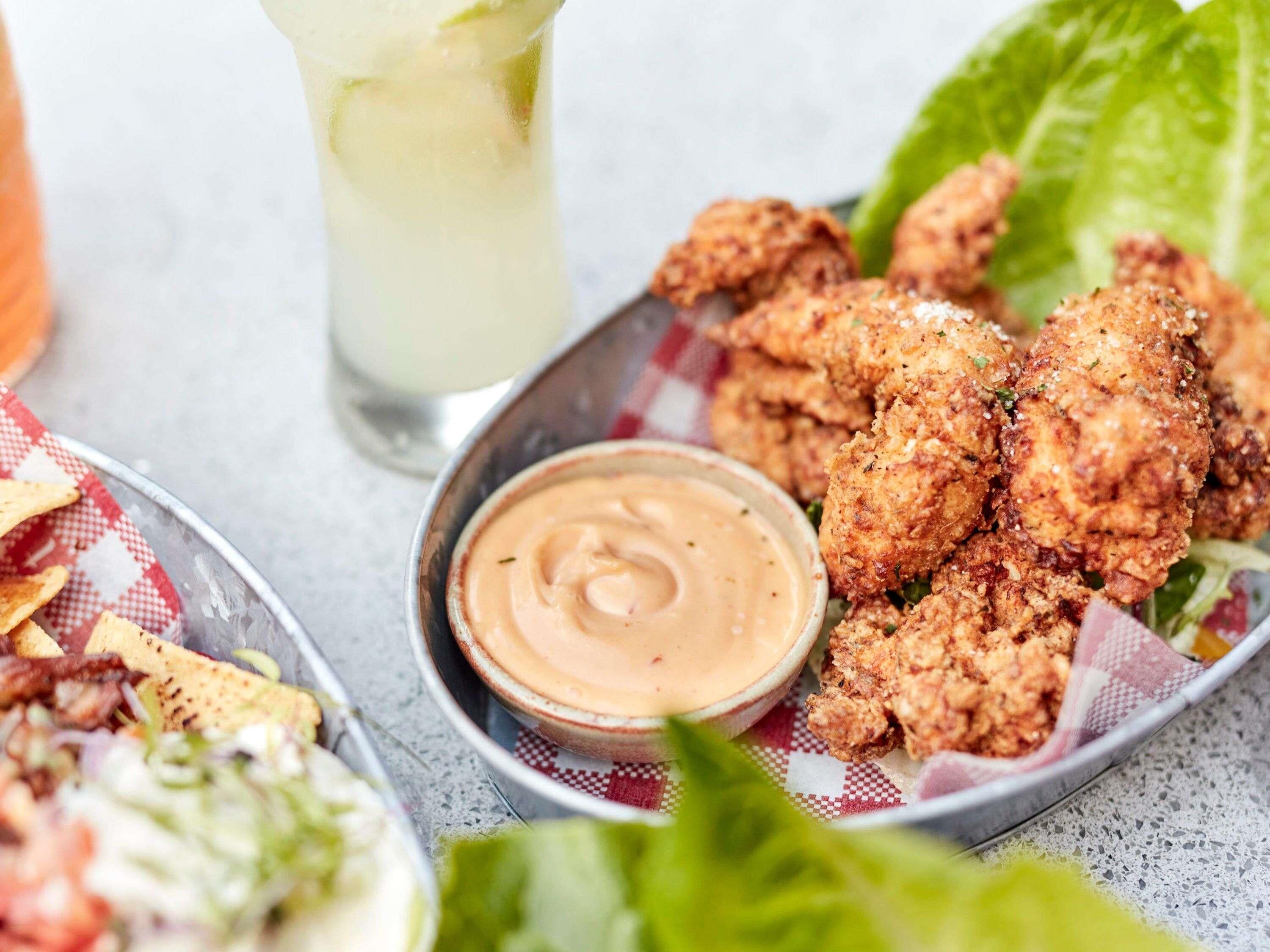 A bowl of fried chicken with dipping sauce and a glass of iced tea.