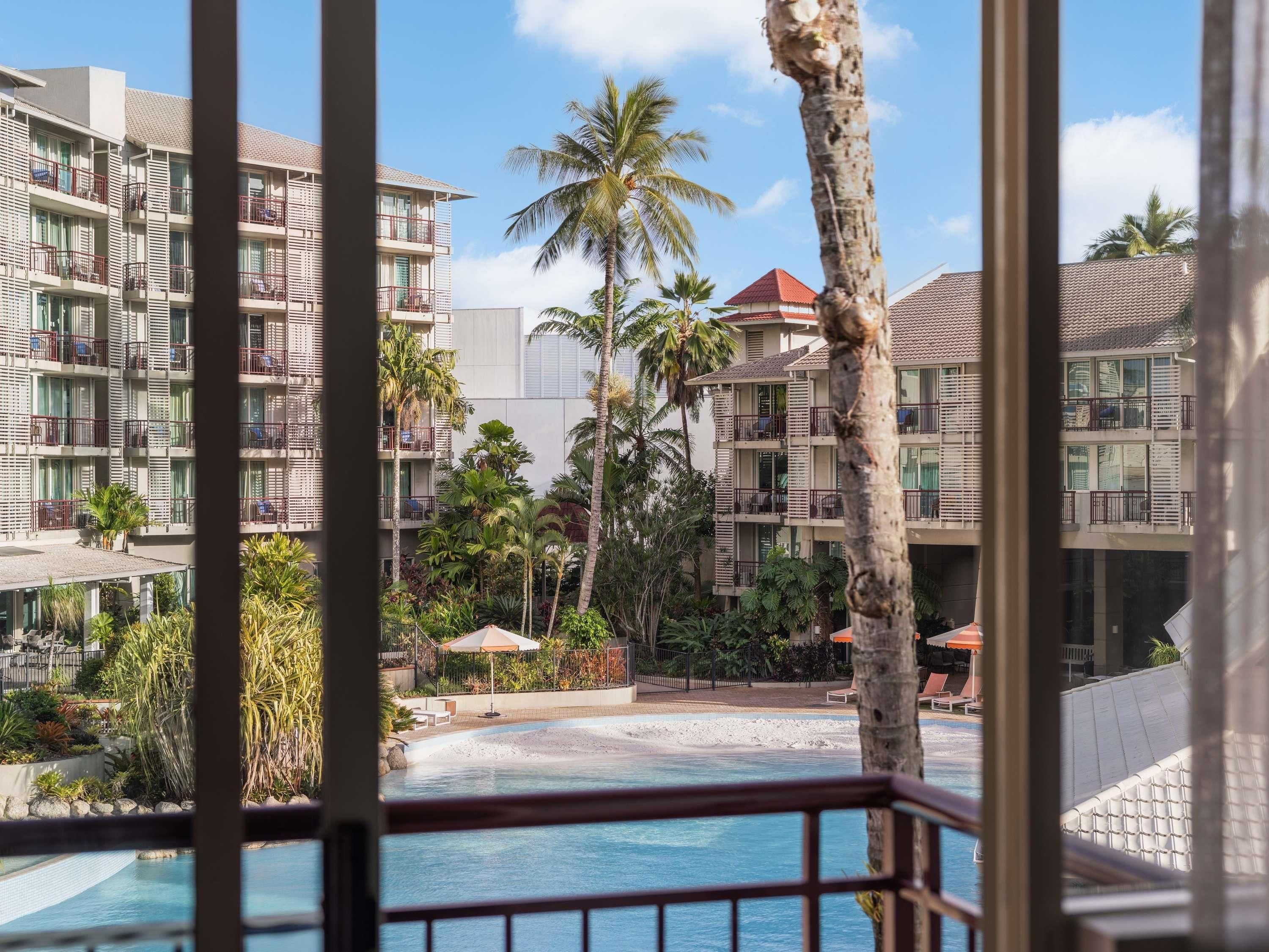 Un hotel de varios pisos, piscinas al aire libre y palmeras.