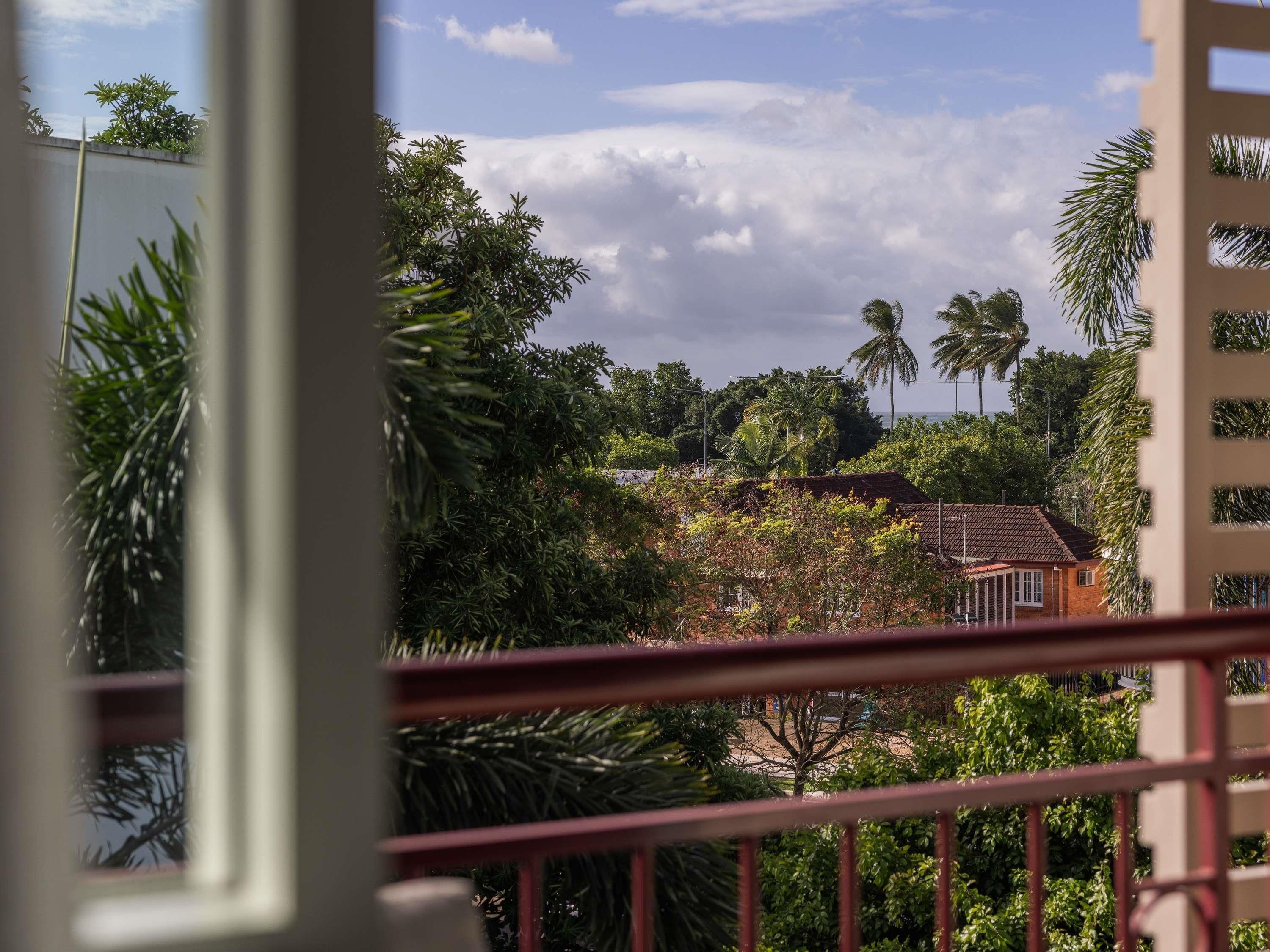 Une vue depuis un balcon doté d’une balustrade, donnant sur un quartier résidentiel avec des maisons, des arbres et un ciel dégagé.