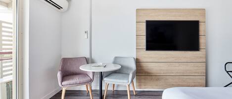 Une chambre d’hôtel moderne équipée d’un lit, d’un téléviseur fixé sur un mur recouvert de panneaux en bois, d’une petite table ronde avec deux chaises et d’un appareil de climatisation.