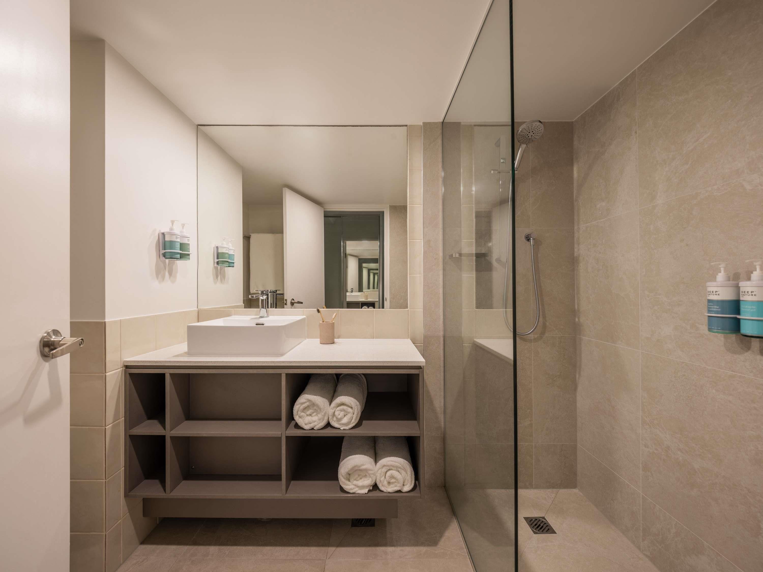 A modern bathroom with a glass shower enclosure, a white sink, and a mirror.