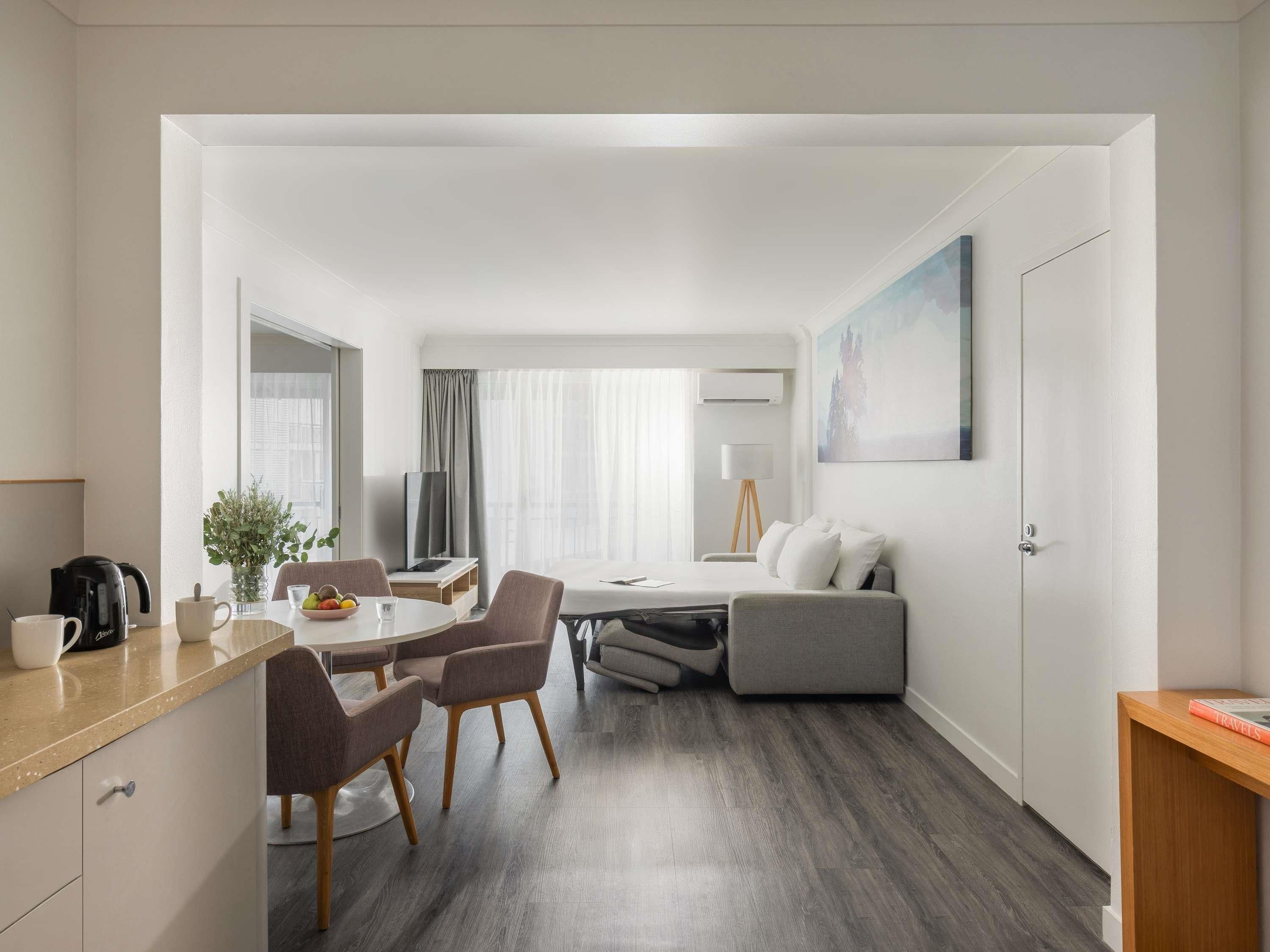 A modern hotel room with a dining area, a sofa, and a bed.