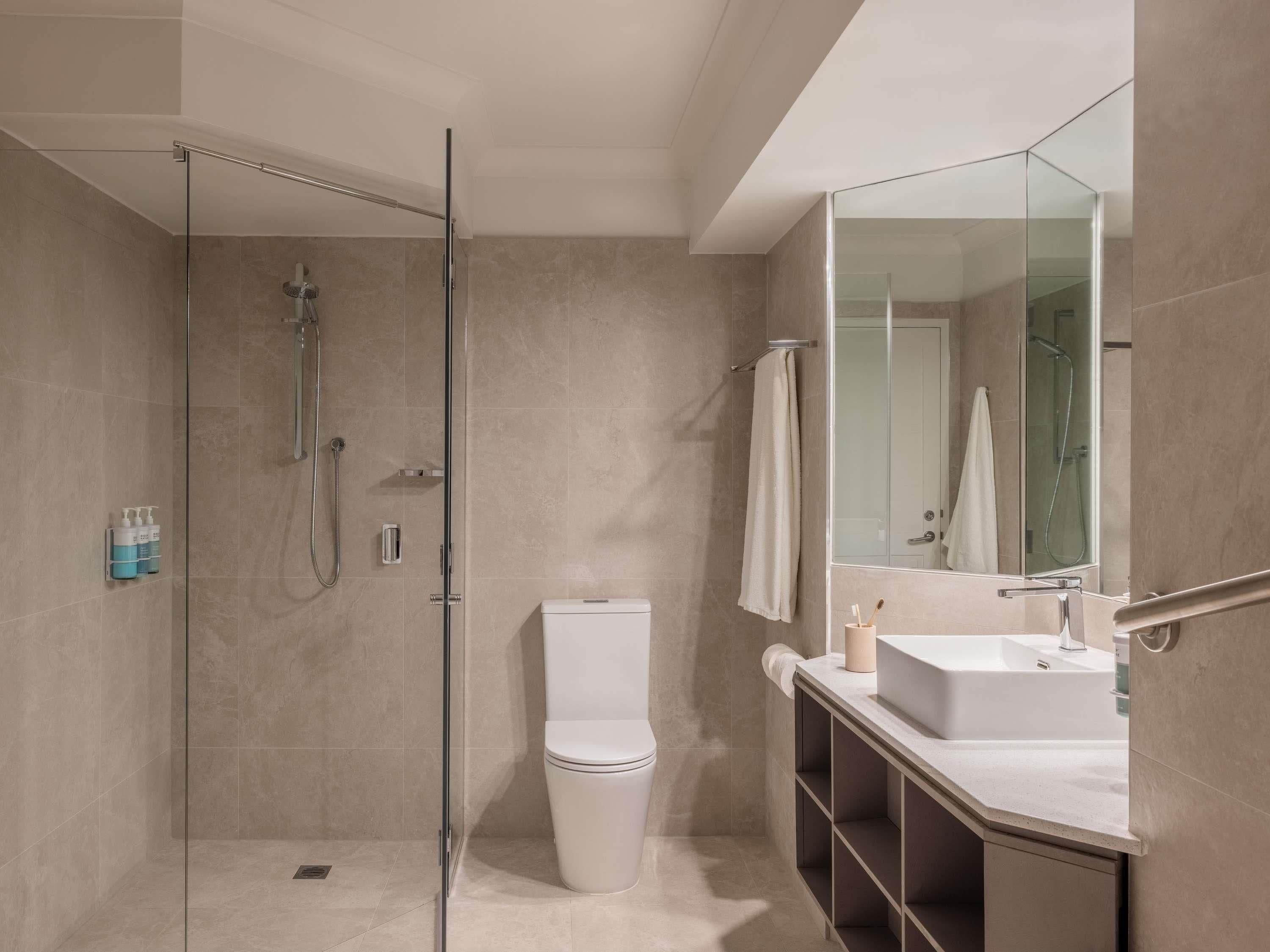 Ein modernes Badezimmer mit einer Duschkabine, Toilette, Waschbecken mit Spiegel und Handtuchhalter.