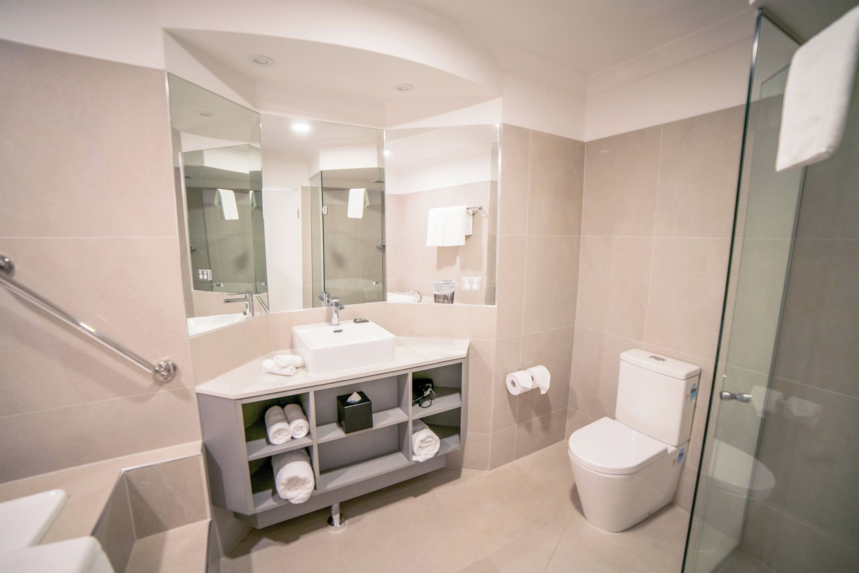 A modern bathroom with a glass shower enclosure, a white sink with a mirror above, and a toilet with a glass partition.