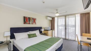 Une chambre d’hôtel avec un lit, un bureau, une chaise, une télévision et une fenêtre avec des rideaux.