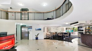 Un hall de hotel con mostrador de recepción, zona de estar y una escalera que sube a un nivel superior.