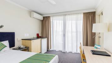 Une chambre d’hôtel avec un lit, un bureau, une chaise et une fenêtre avec des rideaux.