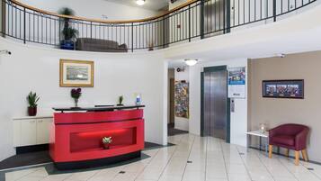 A reception area with a red desk, a white cabinet, a potted plant, a framed picture, and a red chair.