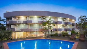 Un hotel de varios pisos con piscina, balcones y mobiliario exterior.