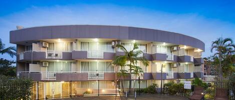 Un hotel de varios pisos con piscina, balcones y mobiliario exterior.