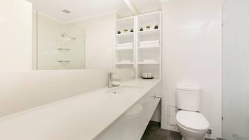 Un baño moderno con un tocador blanco, cabina de ducha de vidrio y un inodoro.