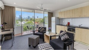 Habitación de hotel moderna con balcón, kitchenette y zona de estar con vista a la ciudad.