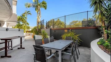 An outdoor patio area with a dining table and chairs, surrounded by potted plants and a railing.