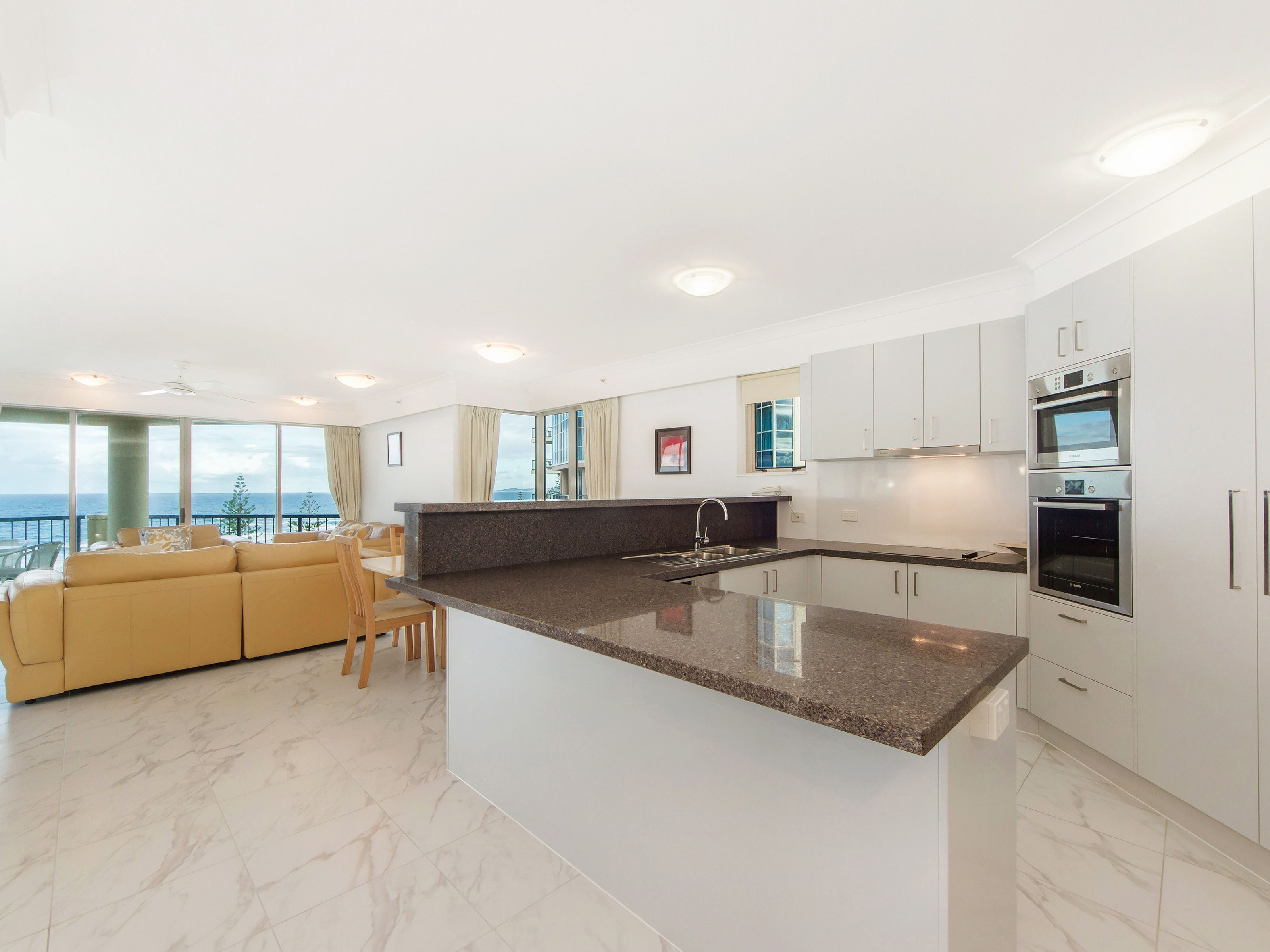 A modern kitchen with a central island, white cabinetry, and built-in appliances.