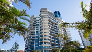 A high-rise hotel with multiple balconies, surrounded by palm trees and other tropical vegetation.