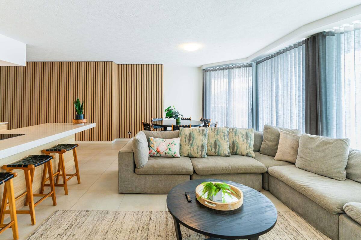 Una sala moderna con un sofá modular, una mesa de centro redonda y una zona de comedor con un separador de madera.