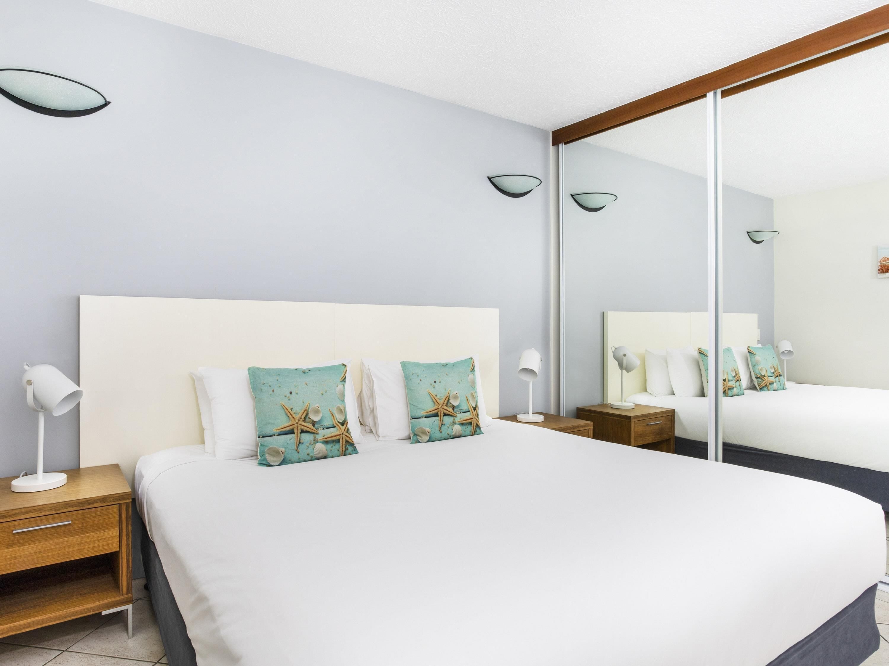 Una habitación de hotel con una cama grande, dos mesitas de noche, un espejo y una lámpara de pared.