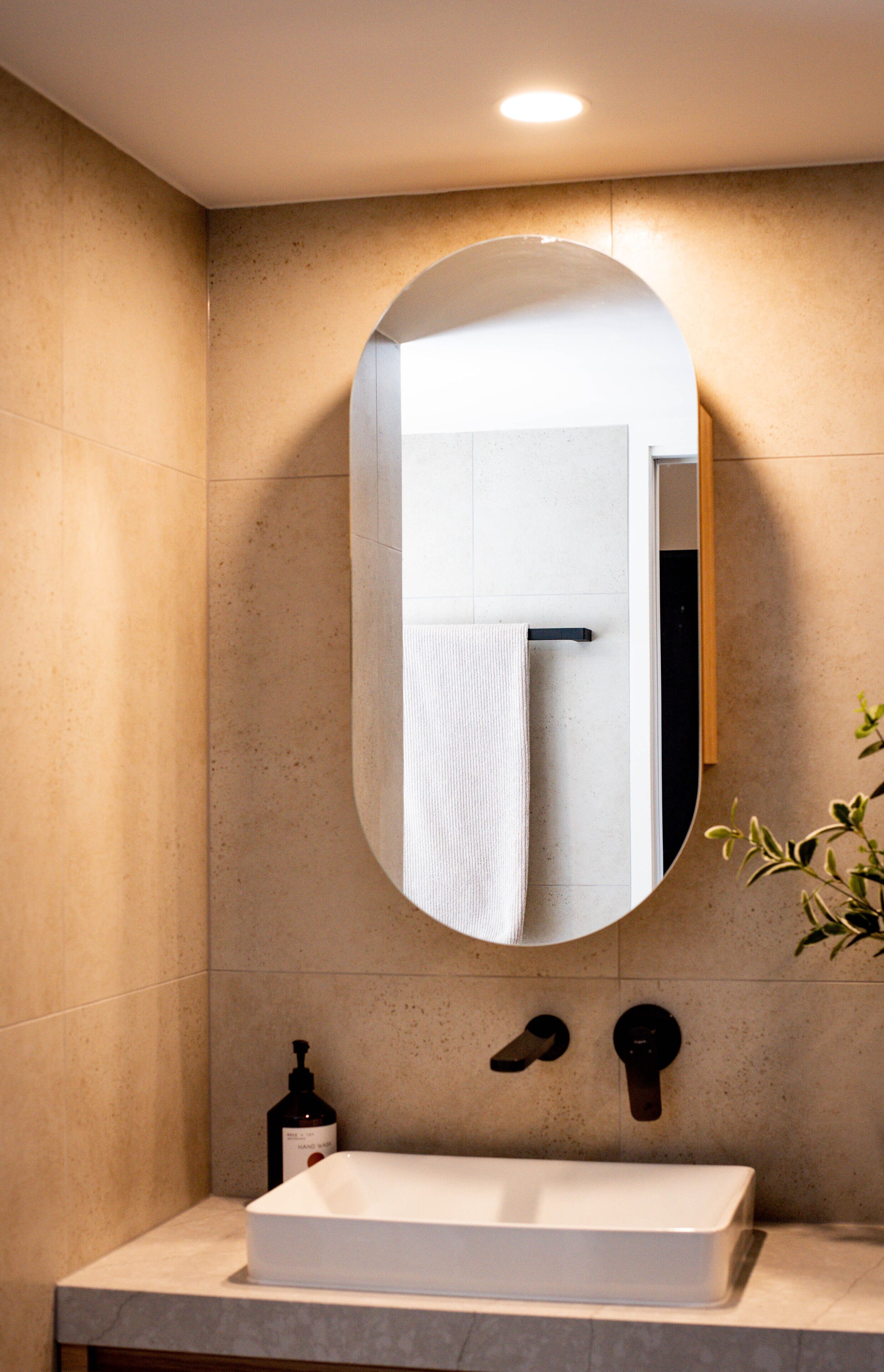 A bathroom with a rectangular sink, a large oval mirror, and a towel rack.