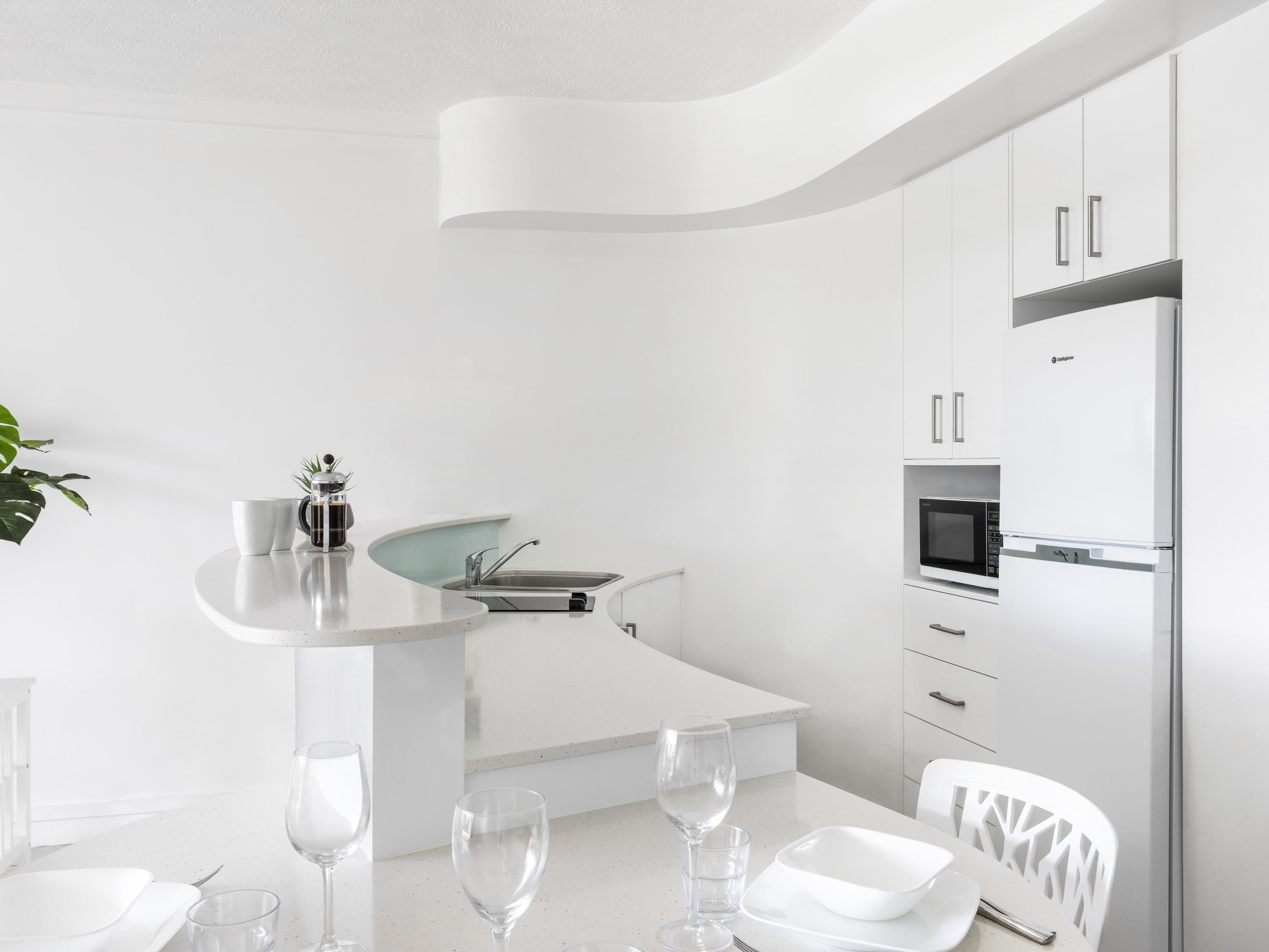 A modern kitchen with white cabinetry, a built-in microwave, and a stainless steel refrigerator.