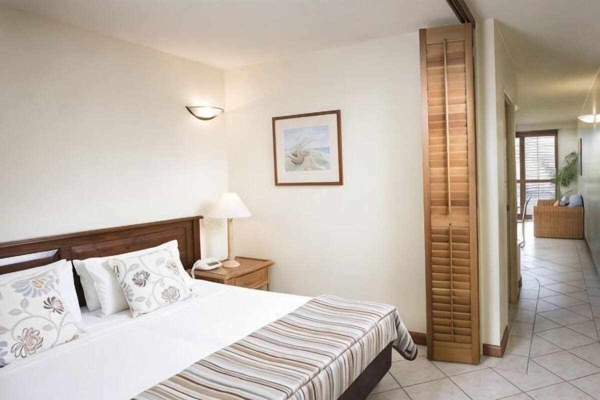 Una habitación de hotel con cama, mesita de noche, lámpara y un cuadro en la pared.
