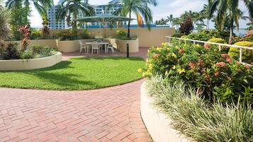 A paved patio area with a brick pattern, surrounded by lush greenery and palm trees.